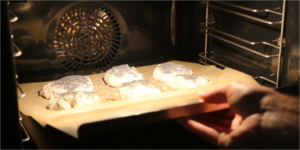 Bagepapir inklusiv boller føres fra kombispaden over på bagestålet i ovnen